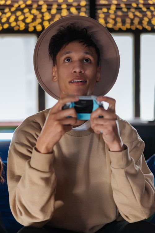 Free A young man wearing a beige sweater and hat intensely plays video games indoors. Stock Photo