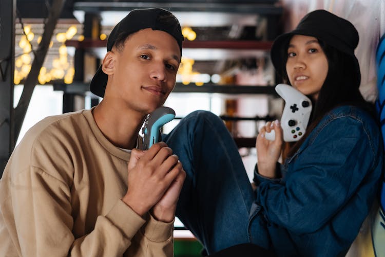 Young Man And Woman Sitting On Steps At Home And Holding Game Controllers