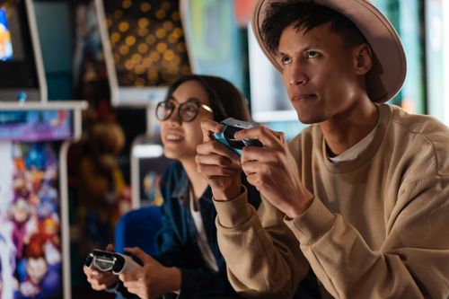 Free Two adults enjoying an immersive gaming session at an arcade, focusing intently on their game controllers. Stock Photo