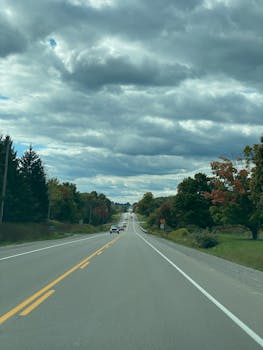 A picturesque road in Port Perry, Ontario, lined with colorful autumn trees under a dramatic cloudy sky.
