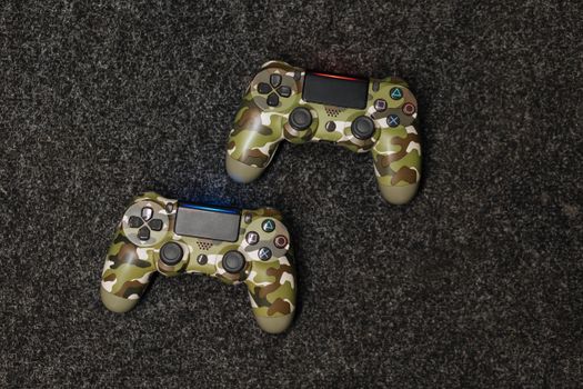 Close-up view of two camouflage-patterned gaming controllers on a textured surface.