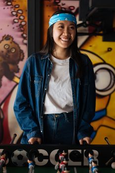 A cheerful woman in denim plays foosball in a retro arcade setting.