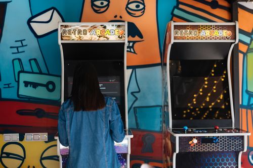 Free Woman engages in retro arcade gaming in a vibrant, graffiti-themed environment. Stock Photo