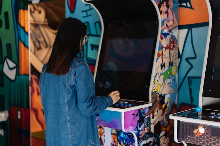 A Girl In A Denim Jacket Playing An Arcade Machine