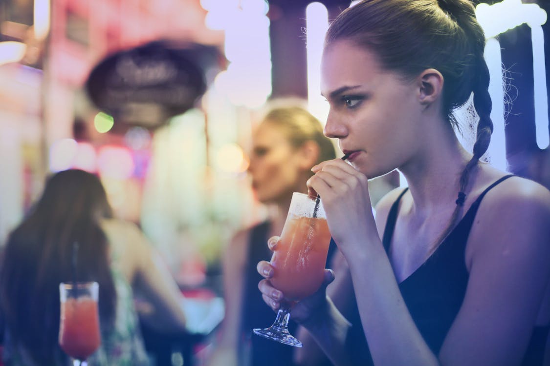 Free 黒のスパゲッティストラップトップと飲み物をすすりながら身に着けている女性 Stock Photo