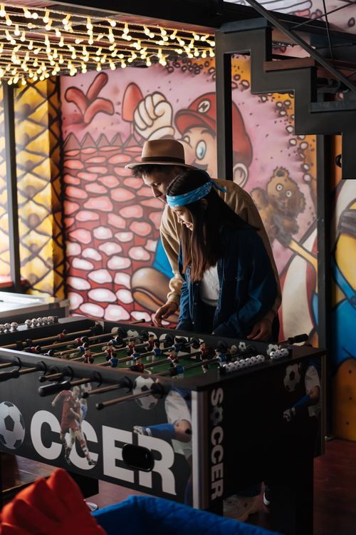 Free A couple having fun playing foosball under colorful lights in a vibrant room. Stock Photo