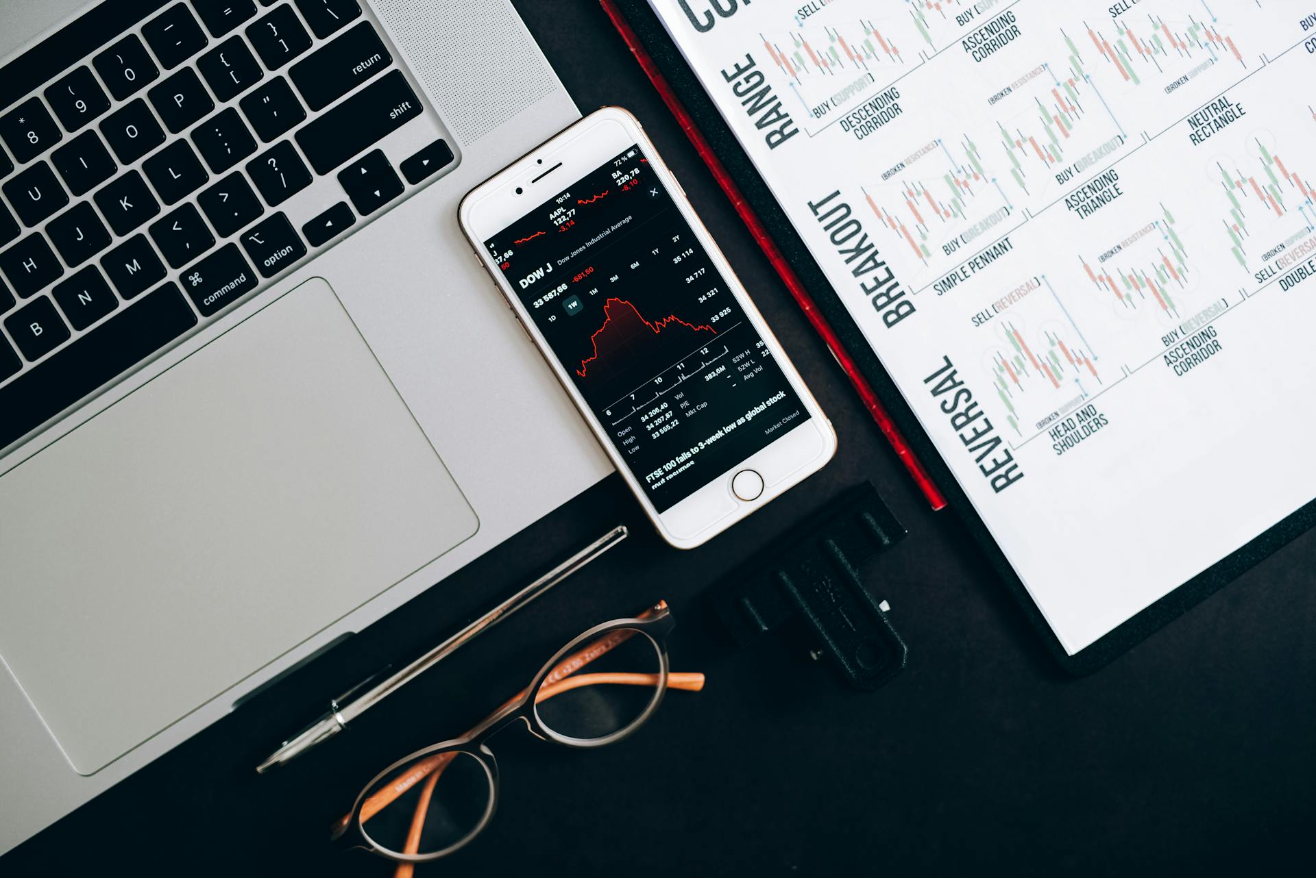 Top view of financial tools including a laptop, smartphone with stock data, and charts for market analysis.