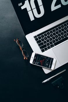 A modern workspace featuring a laptop, smartphone with stock data, and eyeglasses.