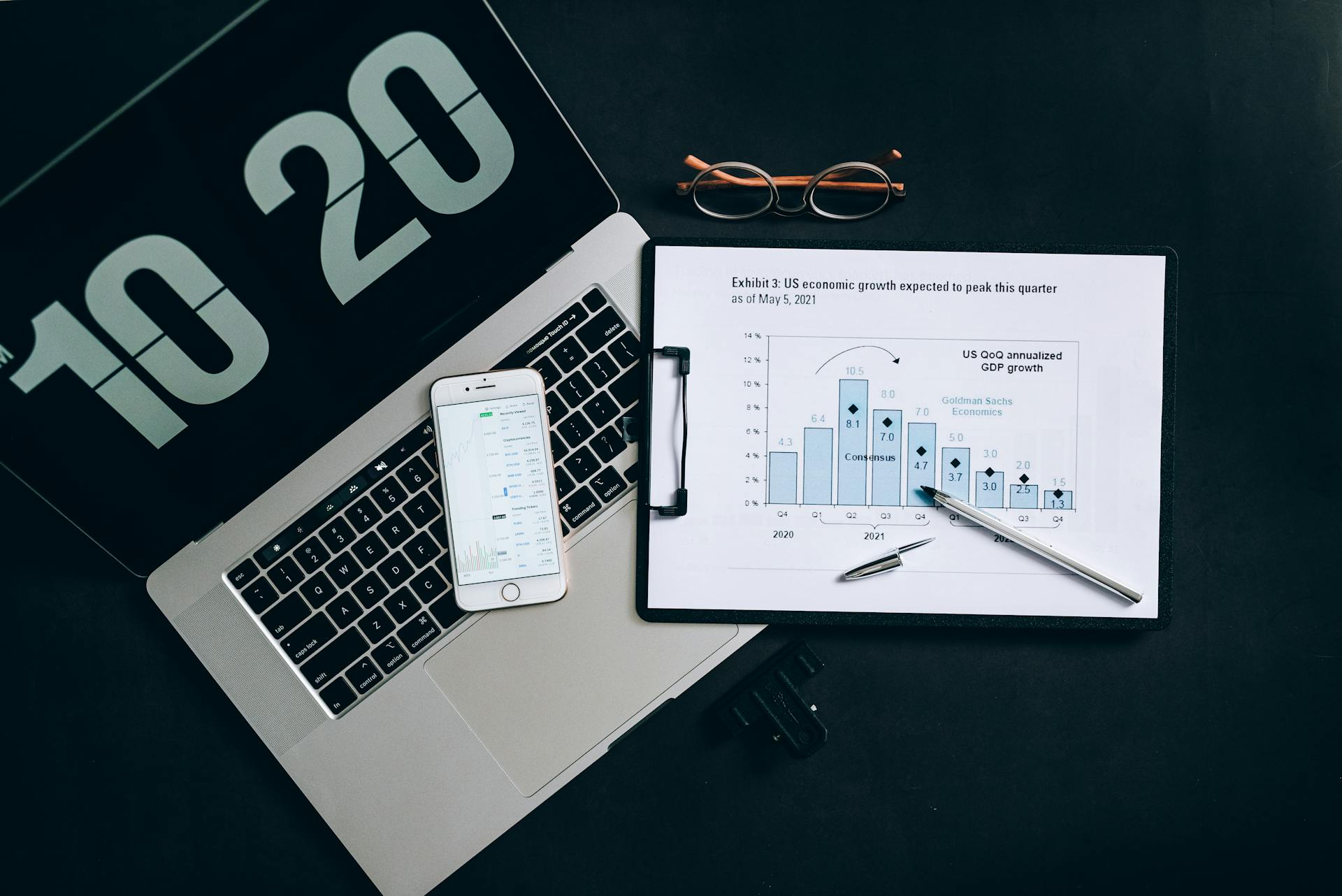 Top view of financial analysis tools on a desk including a laptop, smartphone, and graphs.