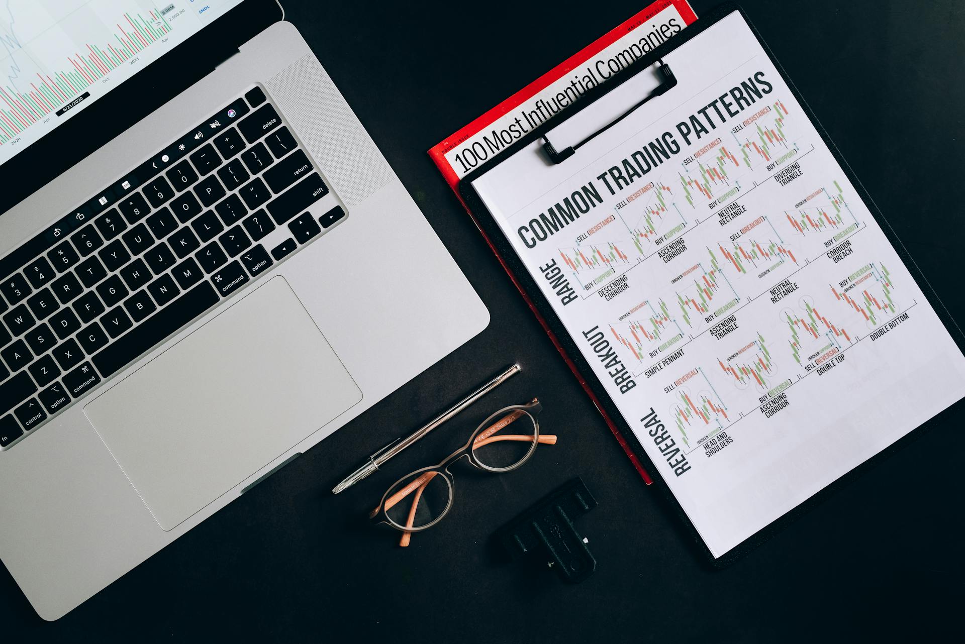 Flat lay of a workspace with trading patterns, charts, and a laptop on a black background, ideal for finance themes.