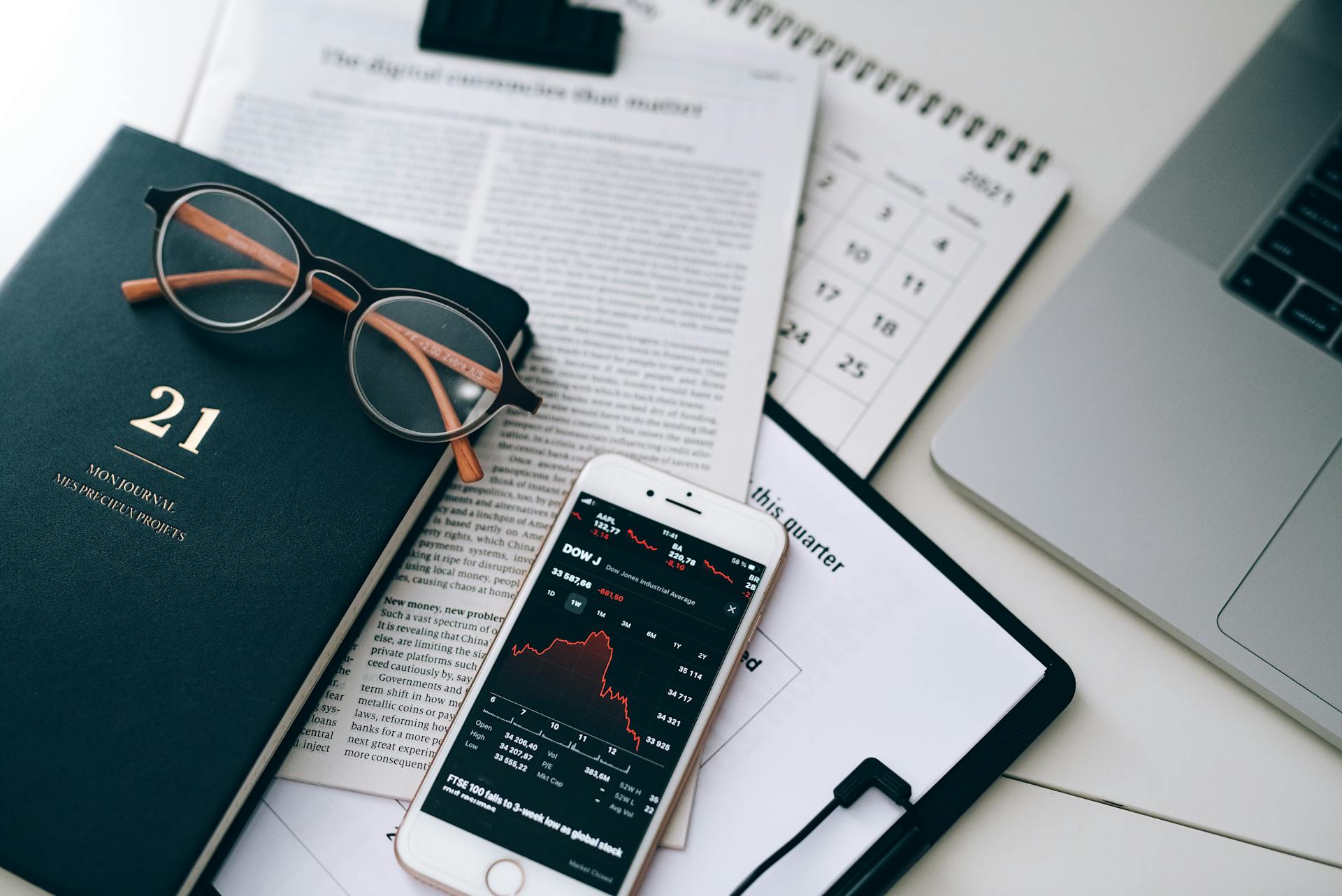 Smartphone Displaying a Stock Market Chart Lying on Documents next to a Laptop on the Desk