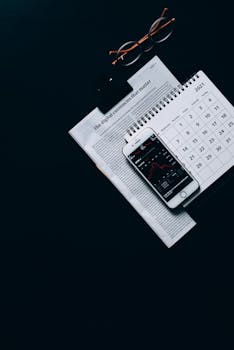 Top view of financial setup with smartphone, calendar, and newspaper on black background.