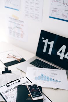 Office workspace featuring financial charts, a digital clock on a laptop, and a smartphone showing stock data.