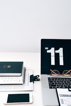 A clean desktop featuring a laptop, smartphone, calendar, and digital clock at 11 AM.
