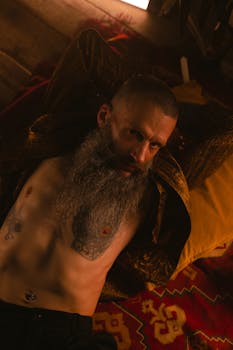 Portrait of a bearded man with tattoos in a warm bohemian setting.