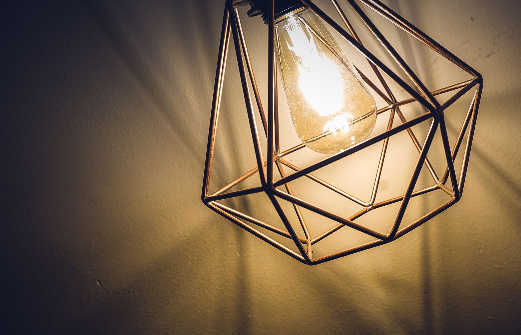 Glowing Edison bulb inside a faceted polyhedral lattice cage casting geometric shadows