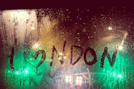 夜晚的雨滴透过一扇雾蒙蒙的窗户，捕捉到城市的灯光，窗上写着“我为伦敦”