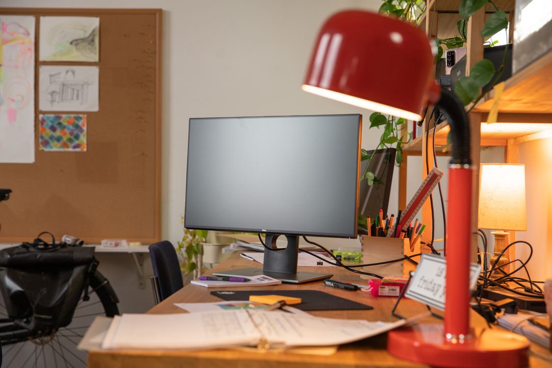 Mesa com monitor, materiais de escritório e luminária vermelha direcionável