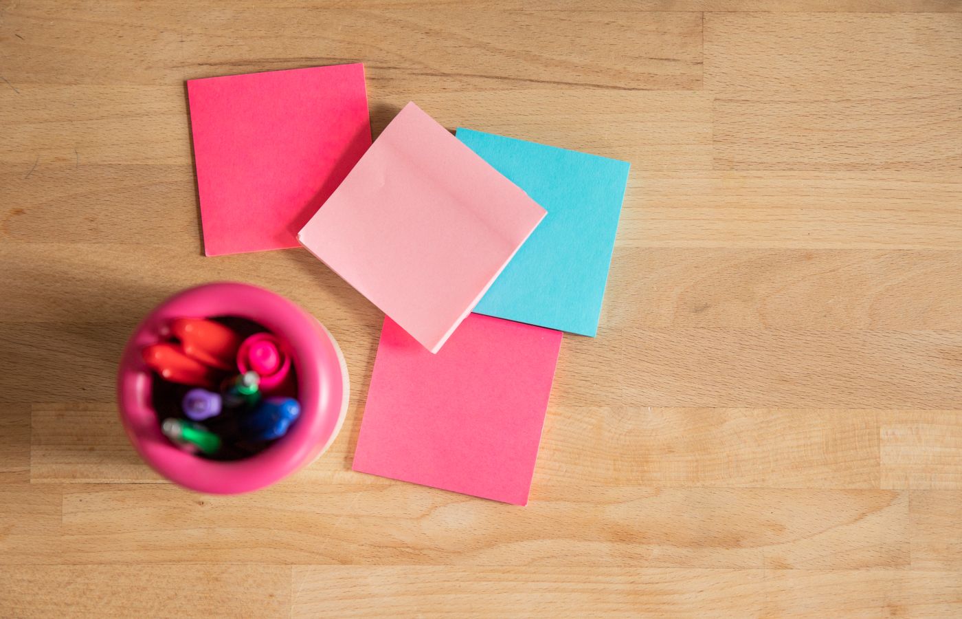 Overhead shot of vibrant sticky notes and pens on a wooden desk.