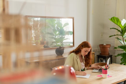 Woman working on laptop and taking notes in a stylish, plant-filled office.