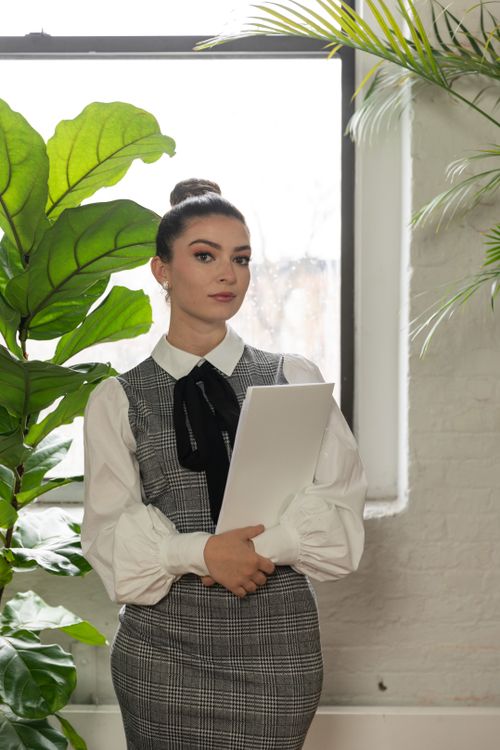 Free Confident woman in a plaid dress and blouse standing in an office with a folder. Stock Photo