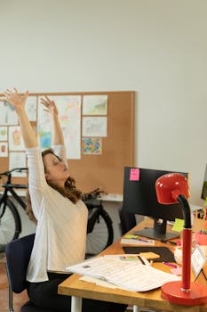 Woman stretches at her office desk, taking a break from work in a modern office setting.