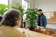 A casual office meeting with a young man in a denim jacket presenting to colleagues.