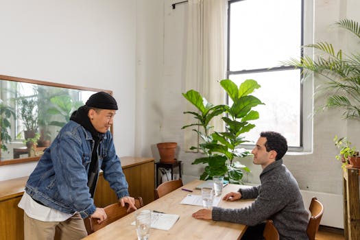 Two coworkers engaged in a focused discussion at a modern office table with plants.
