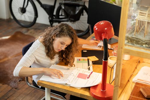 A Woman Reading on a Wooden Table With a Desk Lamp