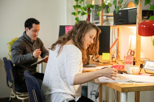 Free Two colleagues working together in a friendly office setting with plants and warm lighting. Stock Photo