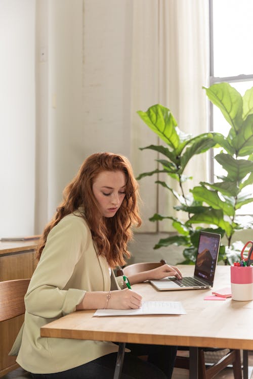 Free Photo of a Woman Typing on Her Laptop while Writing  Stock Photo
