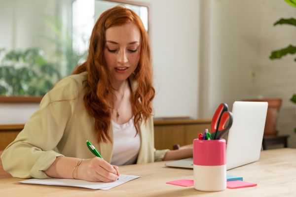 Host writing in a notebook beside a laptop at a wooden desk — photo by RDNE Stock project on Pexels