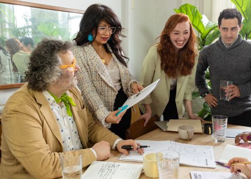 A diverse team collaborates around a table in a light-filled office, exchanging ideas and smiling.