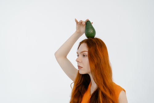 Woman with Orange Hair Holding Avocado on Her Head