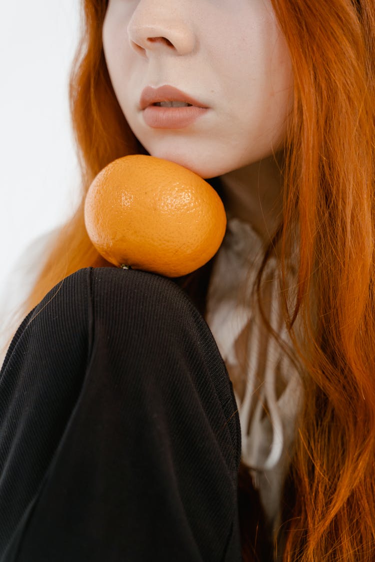 An Orange Fruit Between A Woman's Knee And Chin