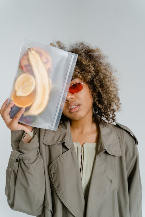 Woman in Gray Coat Holding a Container With Sliced Fruits