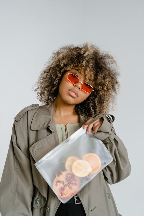 Woman in Brown Coat Holding Slices of Fruits in Clear Plastic Bag