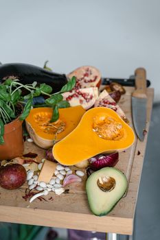 A colorful array of fresh vegetables and fruits including squash, avocado, and pomegranate on a wooden cutting board.