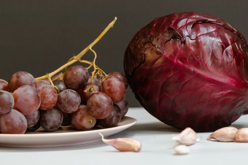 Free A fresh arrangement of red grapes, garlic cloves, and red cabbage on a white plate. Stock Photo