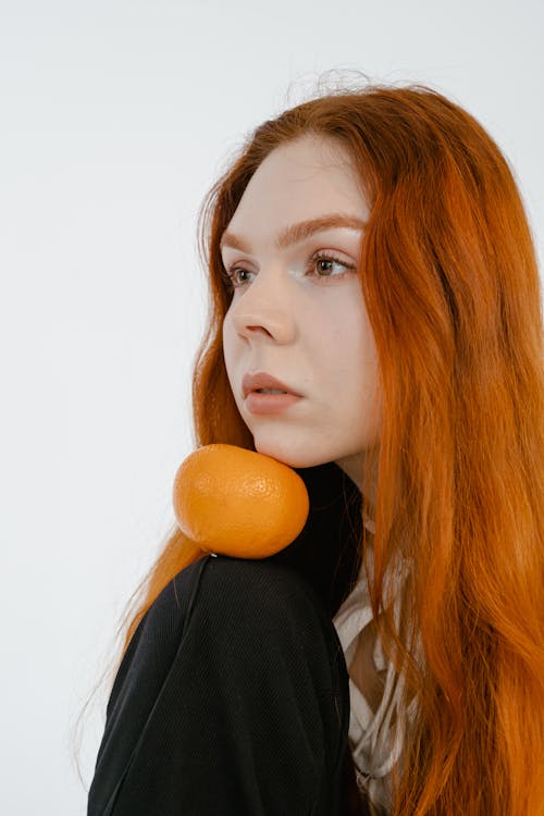 A Woman holding an Orange Fruit on her Chin