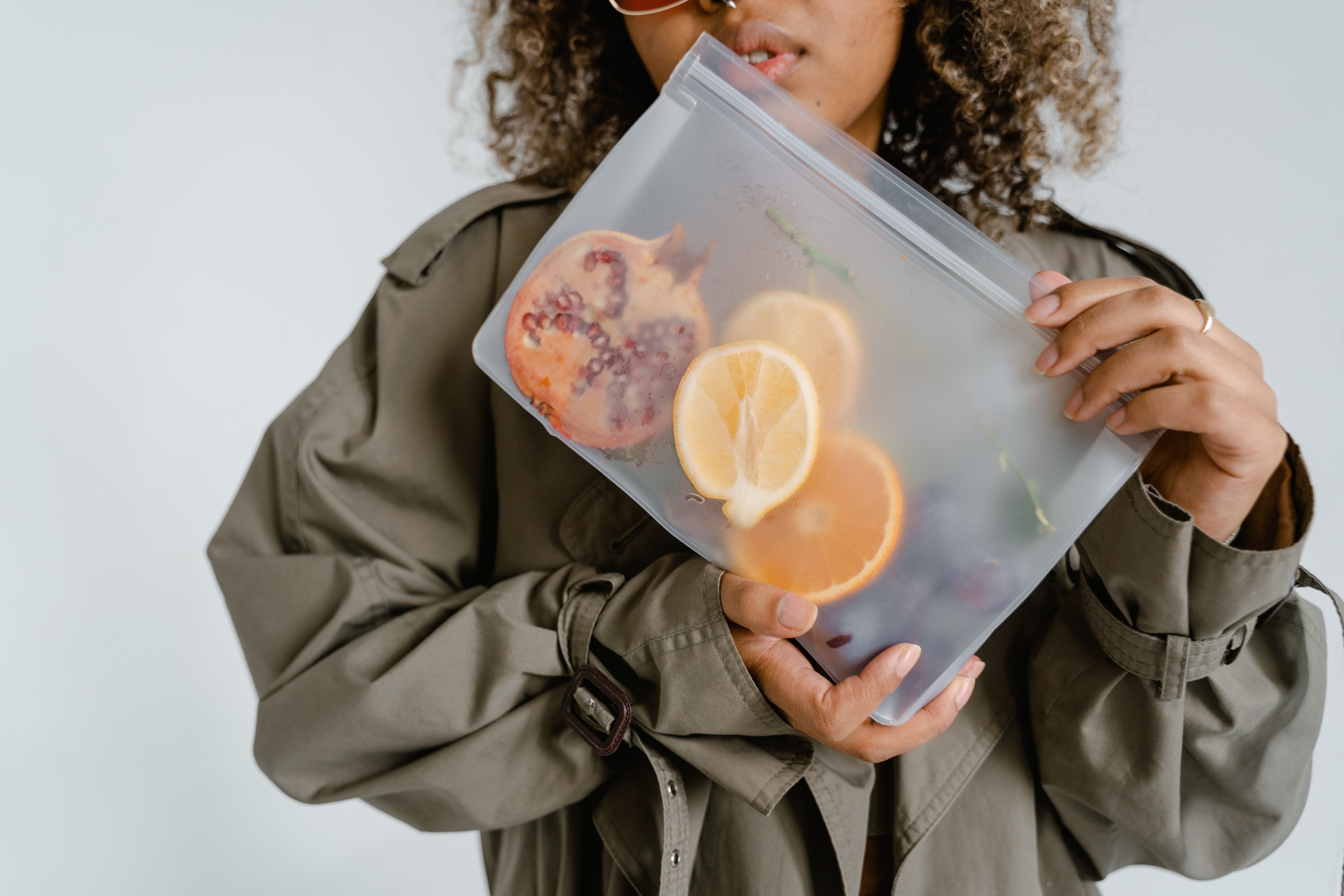 A woman holding a reusable ziplock bag with fresh fruits like lemons and pomegranate.