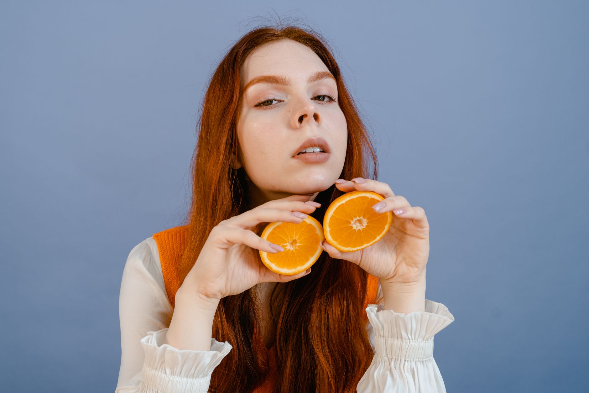 Woman holding orange slices against a blue background in a vibrant portrait.