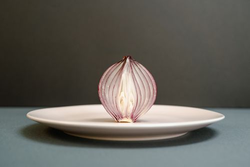 Free A half-sliced red onion creatively displayed on a white plate against a dark backdrop, highlighting detailed textures. Stock Photo