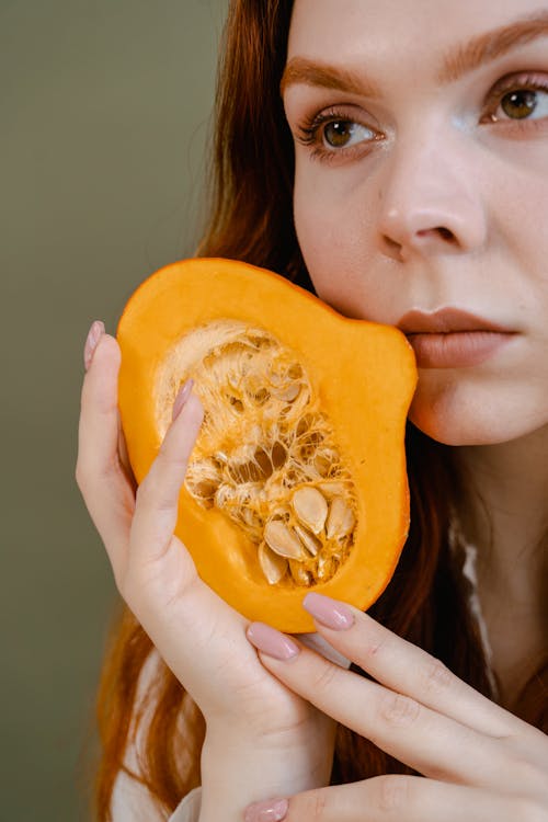 Free A woman holds a pumpkin slice against her face, highlighting natural beauty. Stock Photo