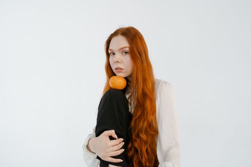Free A woman with long red hair poses with an orange against a plain white background. Stock Photo