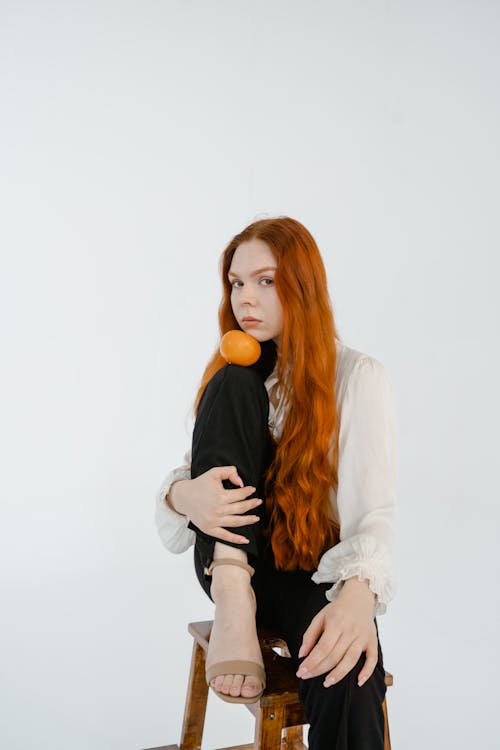 Studio Shot of a Young Woman Sitting on a Chair on White Background and Holding a Tangerine 