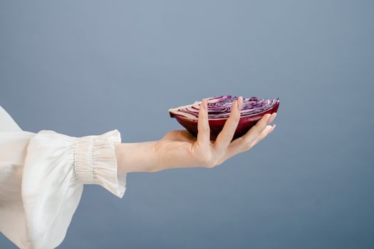 A woman's hand gracefully holds a sliced red cabbage against a blue background, symbolizing freshness and health.