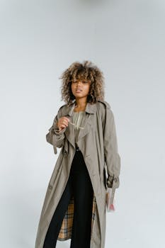 Fashionable woman posing confidently in a trench coat against a simple white backdrop, showcasing modern style.