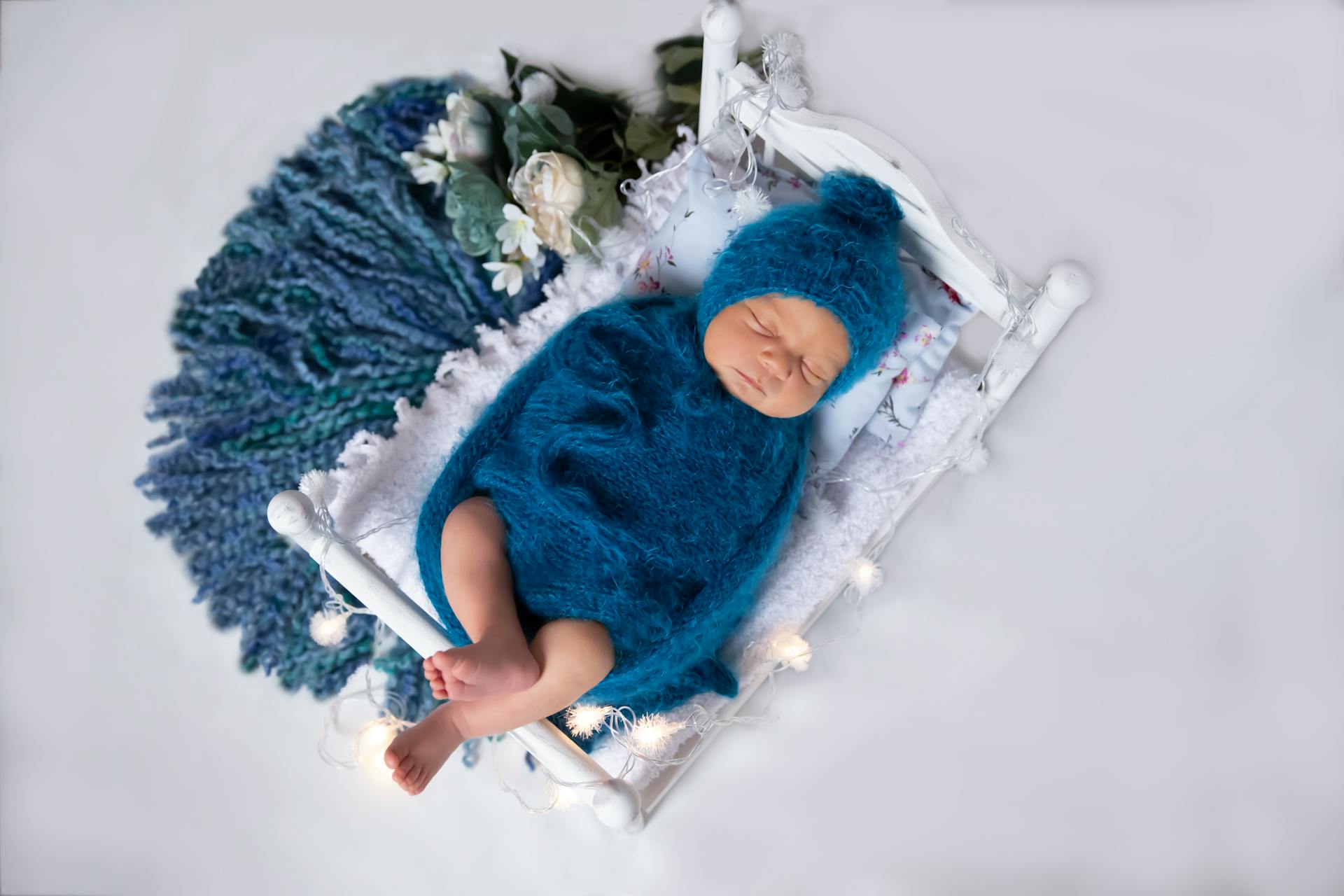 Peaceful baby sleeping in a blue wrap on a miniature bed with a cozy setup.
