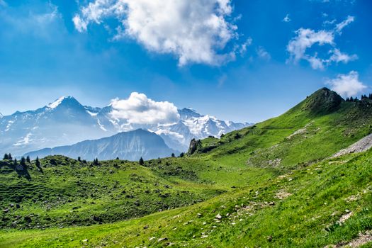 Majestic view of green hills and snow-capped mountains beneath a vibrant blue sky.